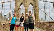 A group of five people are posing for a photo on the Brooklyn Bridge with the New York City skyline in the background.