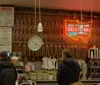 Customers await service at a deli counter adorned with hanging salamis and a neon Send a Salami sign