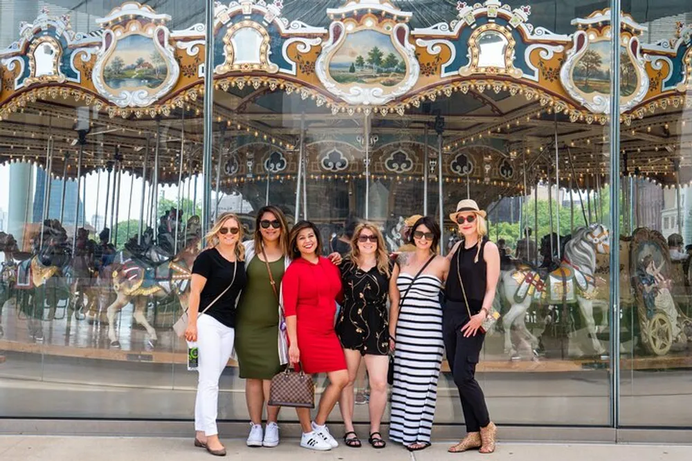 A group of six women is posing for a photo in front of a carousel with ornate decorations