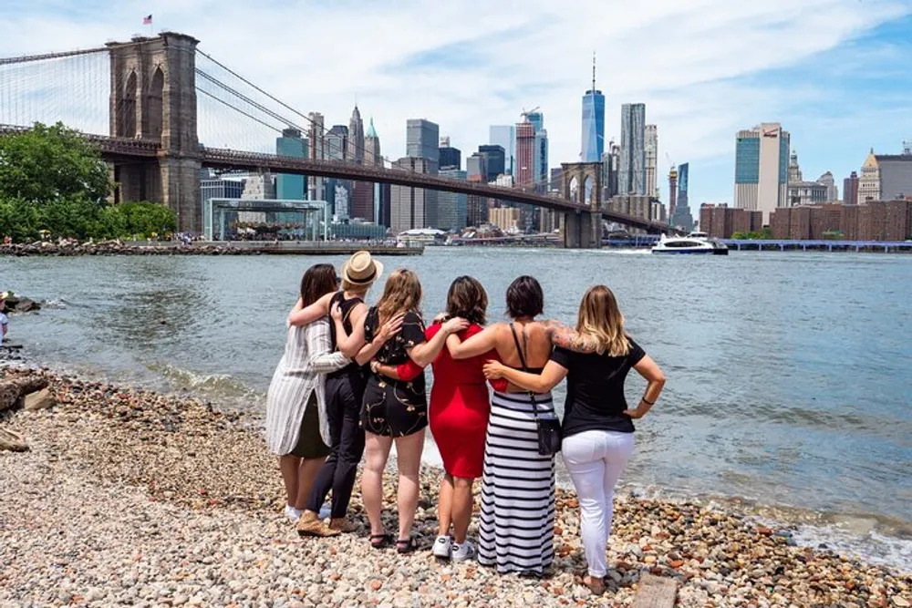 A group of people are embracing while enjoying a view of the Brooklyn Bridge and the New York City skyline