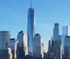 The image shows a clear view of the Lower Manhattan skyline dominated by the One World Trade Center under a blue sky
