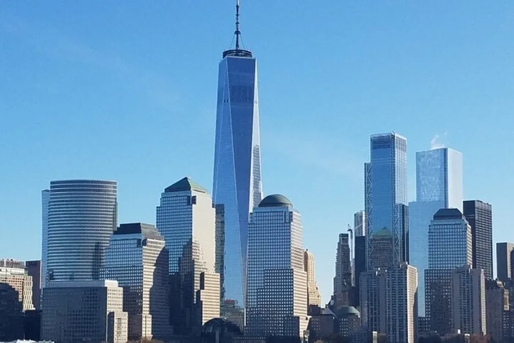 The image shows a clear view of the Lower Manhattan skyline dominated by the One World Trade Center under a blue sky