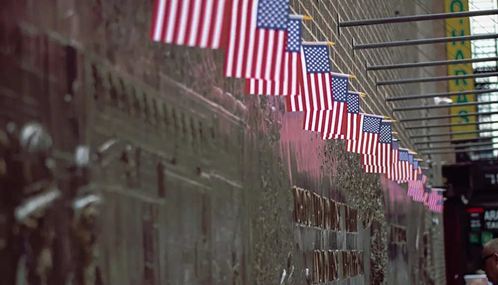 A line of American flags is hung against a wall filled with tribute messages reflecting a somber and respectful atmosphere