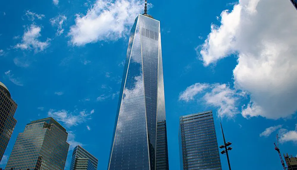 The image shows a towering skyscraper reaching into a blue sky dotted with clouds surrounded by other high-rise buildings