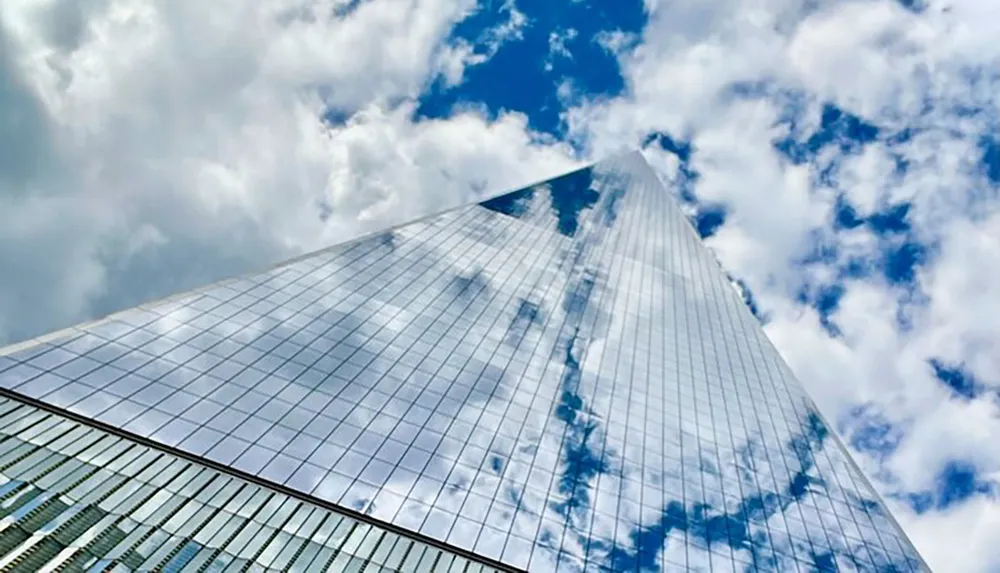 A glass skyscraper reflecting the clouds and blue sky towers above creating an illusion of continuity with the heavens