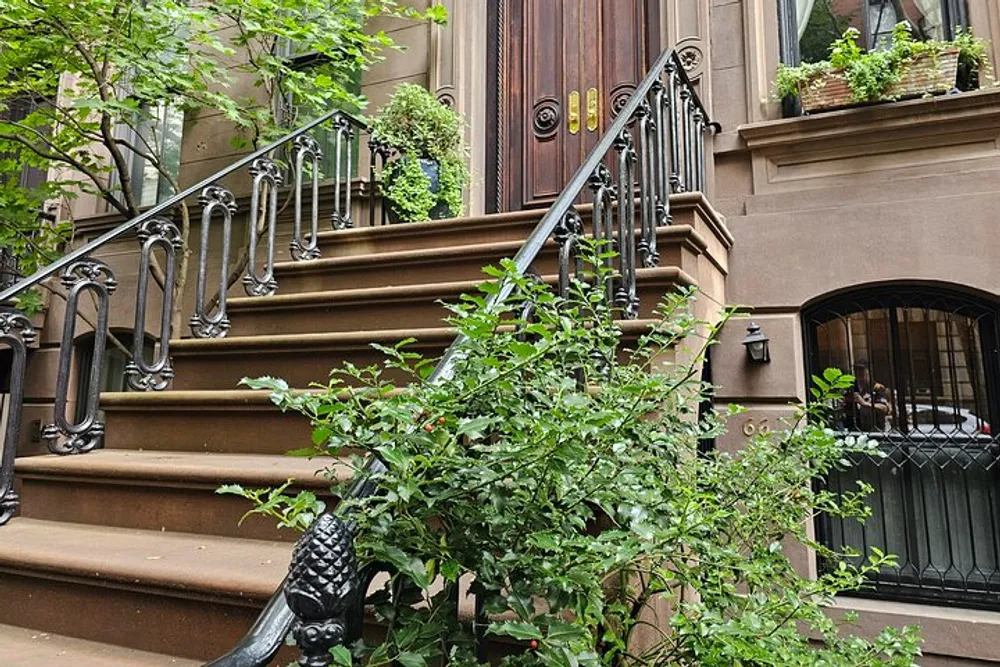 The image shows the front steps of a New York City brownstone with ornate iron railings and greenery capturing a quintessential urban residential scene