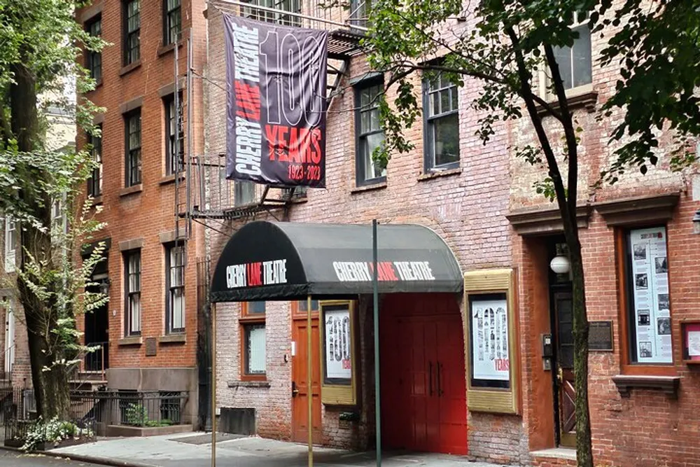 The image shows the facade of the Cherry Lane Theatre with a banner celebrating its 100th anniversary from 1923-2023