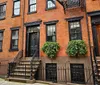 The image shows the front steps of a New York City brownstone with ornate iron railings and greenery capturing a quintessential urban residential scene