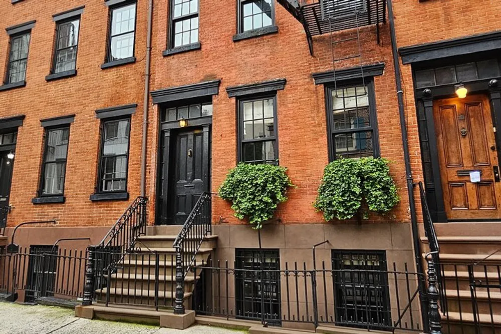 The image shows a charming brick townhouse with green window planters a classic stoop with wrought iron railings and a traditional wooden front door