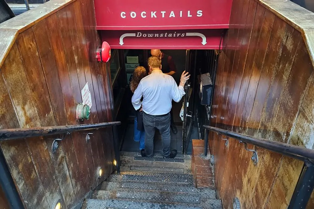 A person is entering a cocktail bar located downstairs as indicated by the signage above the stairway