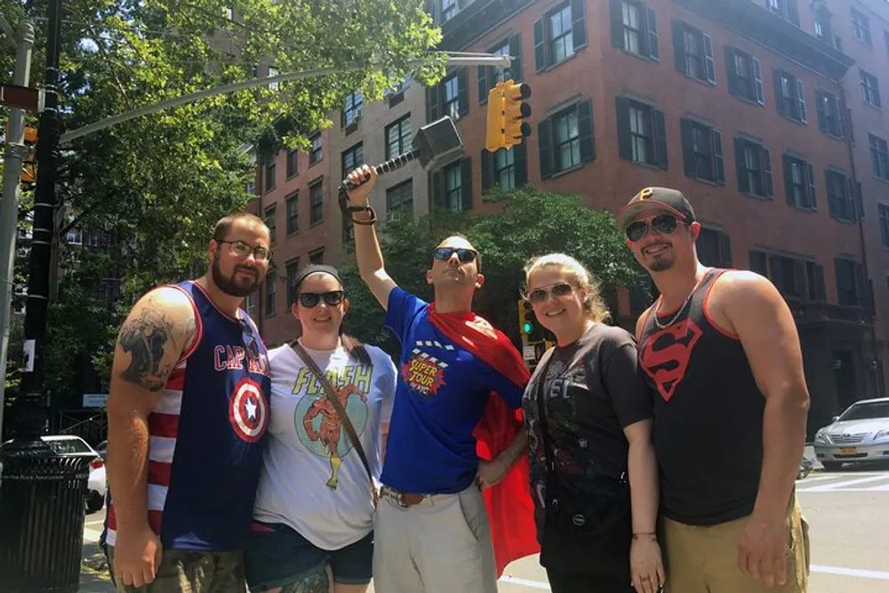 A group of five people wearing superhero-themed clothing is posing with smiles on a sunny street corner