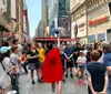 A cheerful person dressed in a superhero-style outfit with a cape is posing in front of a colorful bus advertising The Super Tour of NYC