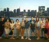 A group of people is posing for a photo on a waterfront with a city skyline illuminated at dusk in the background