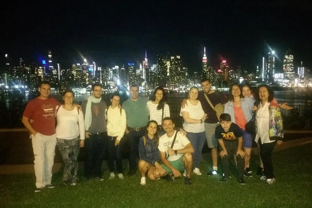 A group of people is posing for a photo at night with a brightly lit city skyline in the background