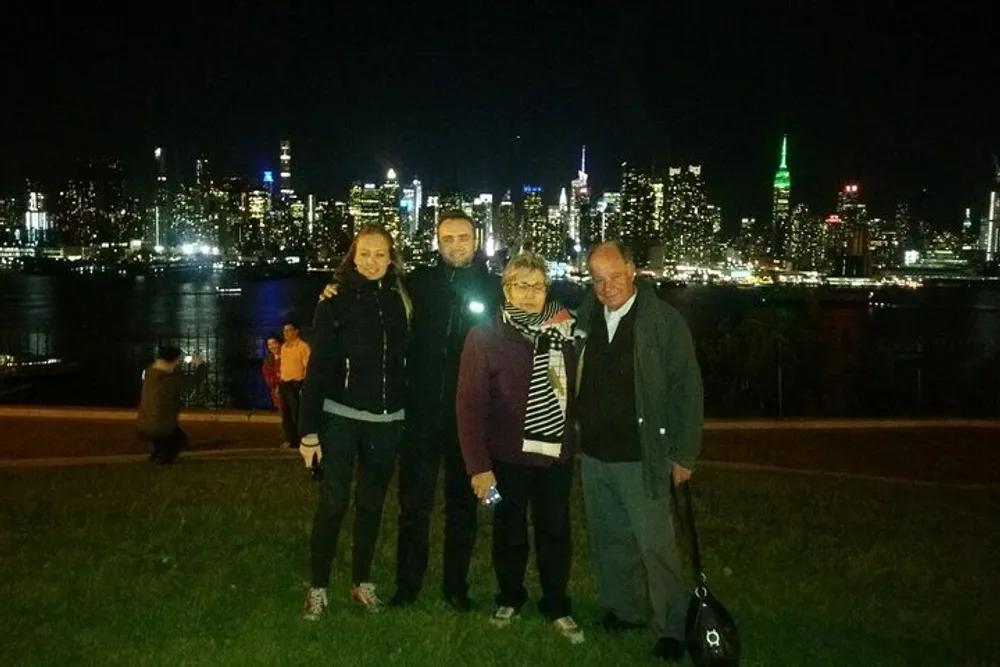 Four people are posing for a photo at night with a brightly lit city skyline in the background