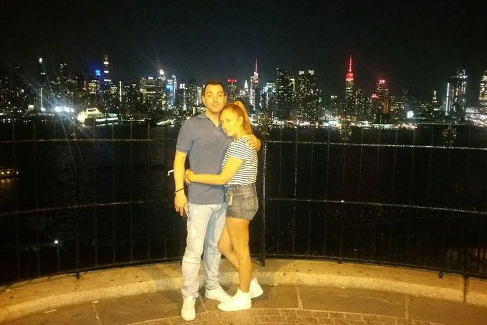 A couple is embracing in front of a vibrant city skyline at night