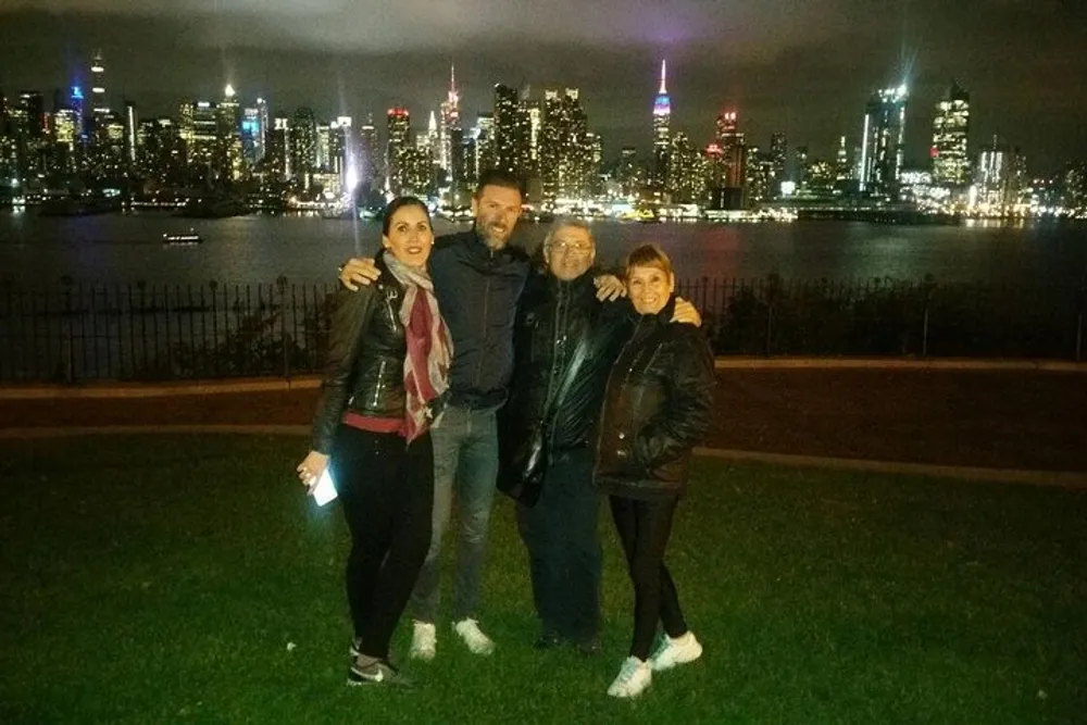 Three people are posing for a photo at night with a vibrant city skyline illuminated in the background
