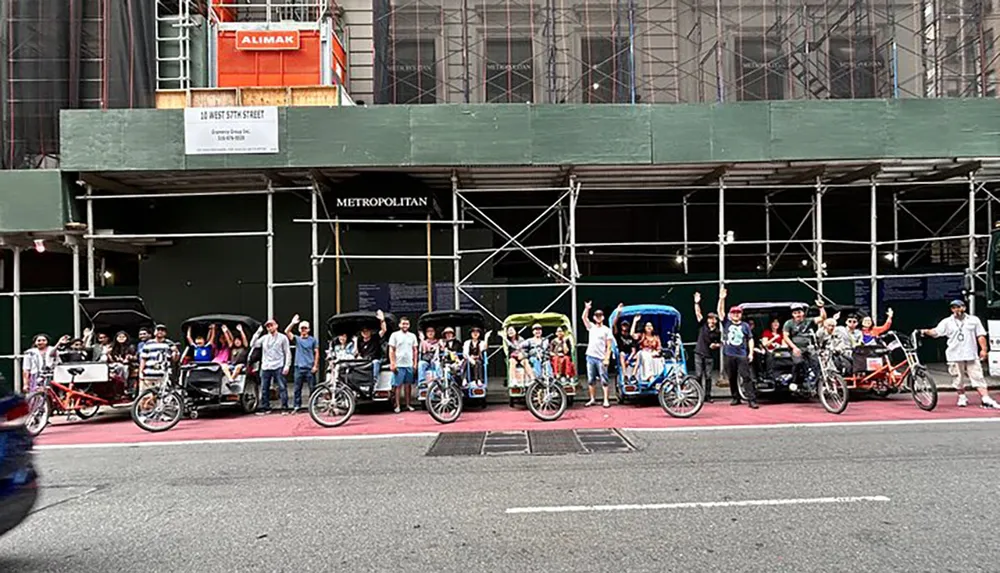 A group of pedicab drivers and their passengers are posing for a photo on a city street with their vehicles