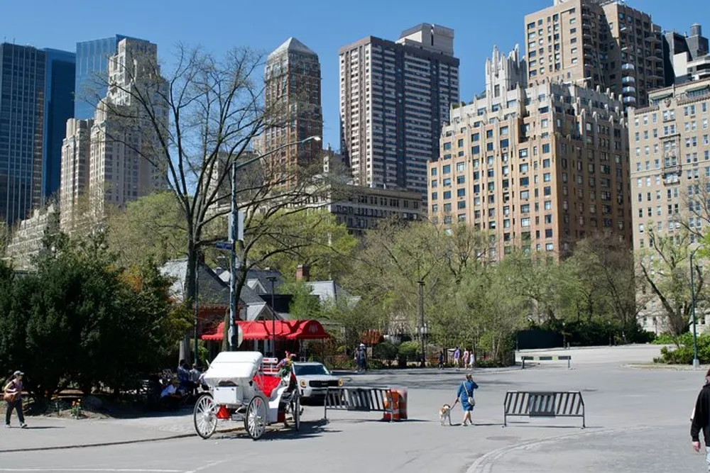 A horse-drawn carriage waits by the roadside in a sunny park with towering buildings in the backdrop