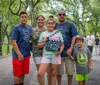 A happy family of five is posing for a photo while enjoying a day out in what appears to be Central Park with the youngest member holding a guidebook