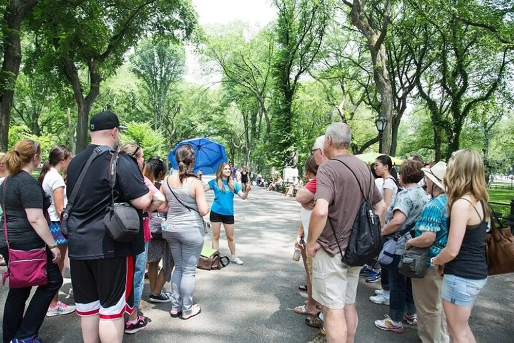 A group of people is attentively listening to a guide during an outdoor walking tour in a lush green park