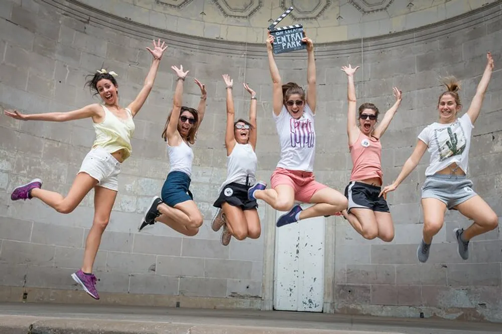 Six people are joyfully jumping in the air in front of a Central Park sign