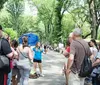 A group of people is gathered around a tour guide holding a blue umbrella in a park-like setting