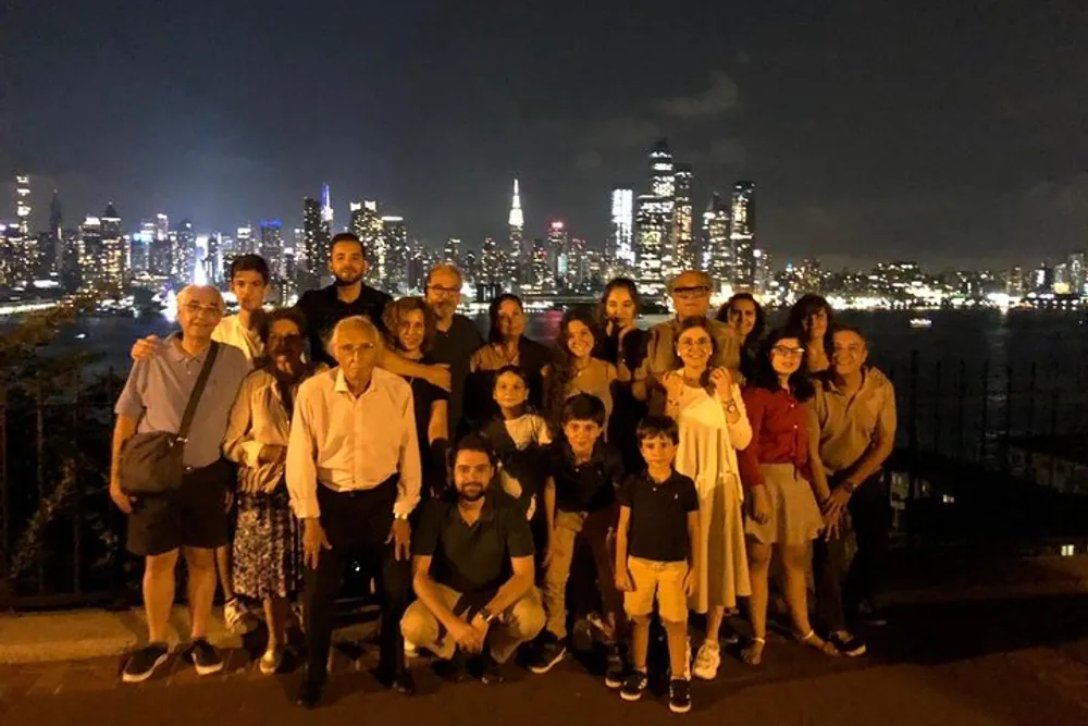 A group of people pose for a nighttime photo with a brightly lit city skyline in the background