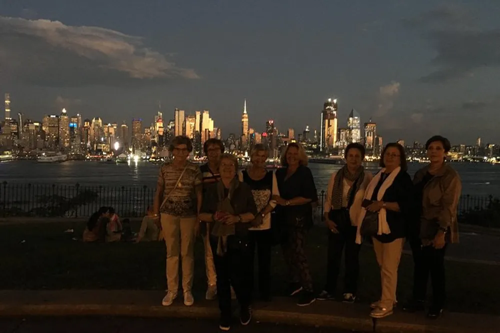 A group of people is posing for a photo with the illuminated skyline of a city at dusk in the background