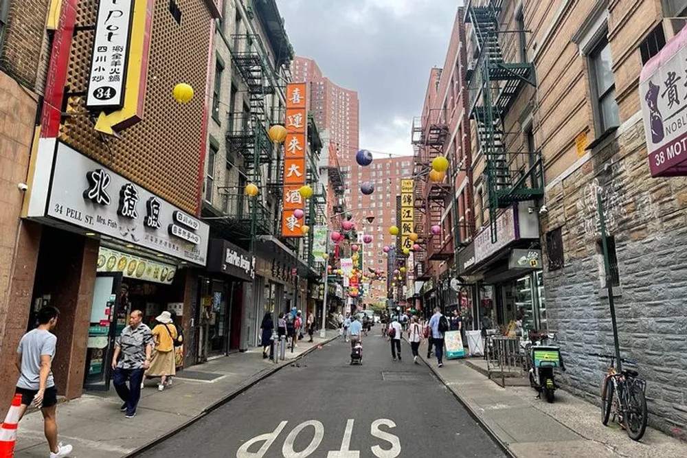 A vibrant street scene with pedestrians adorned with colorful hanging lanterns and lined with storefronts showcasing Chinese characters likely depicting a Chinatown district