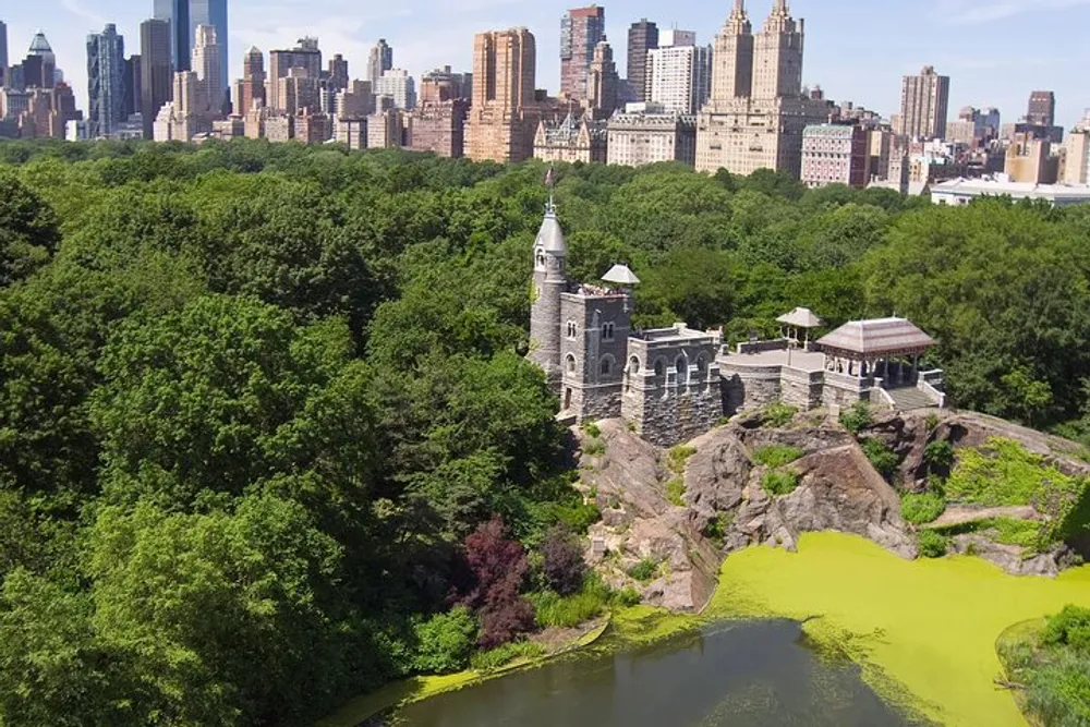 The image captures a historic stone building overlooks a vibrant green pond within a lush park with the skyline of a bustling city in the background