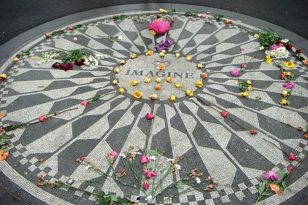 A mosaic with the word IMAGINE at the center is adorned with scattered flowers as a tribute