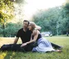 A man and a woman are smiling and posing closely together in a sunlit park