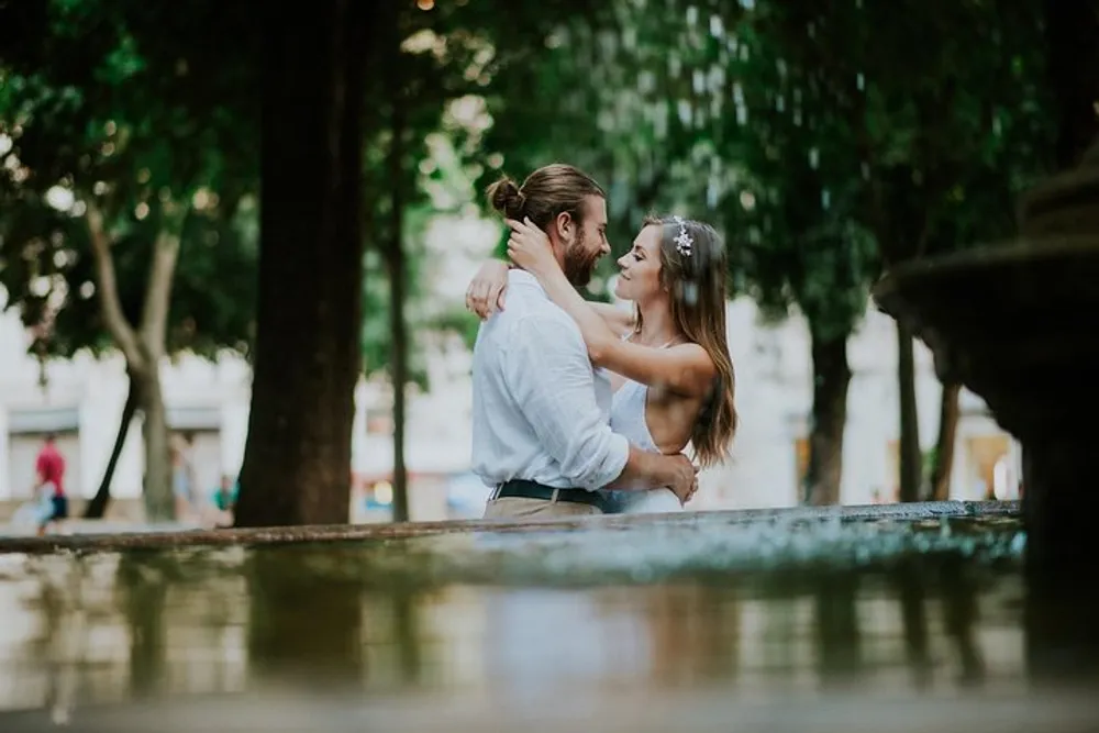 A couple is sharing an intimate embrace near a fountain in a park setting