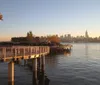 The image shows a serene waterfront pathway at sunset with a view of a city skyline in the background