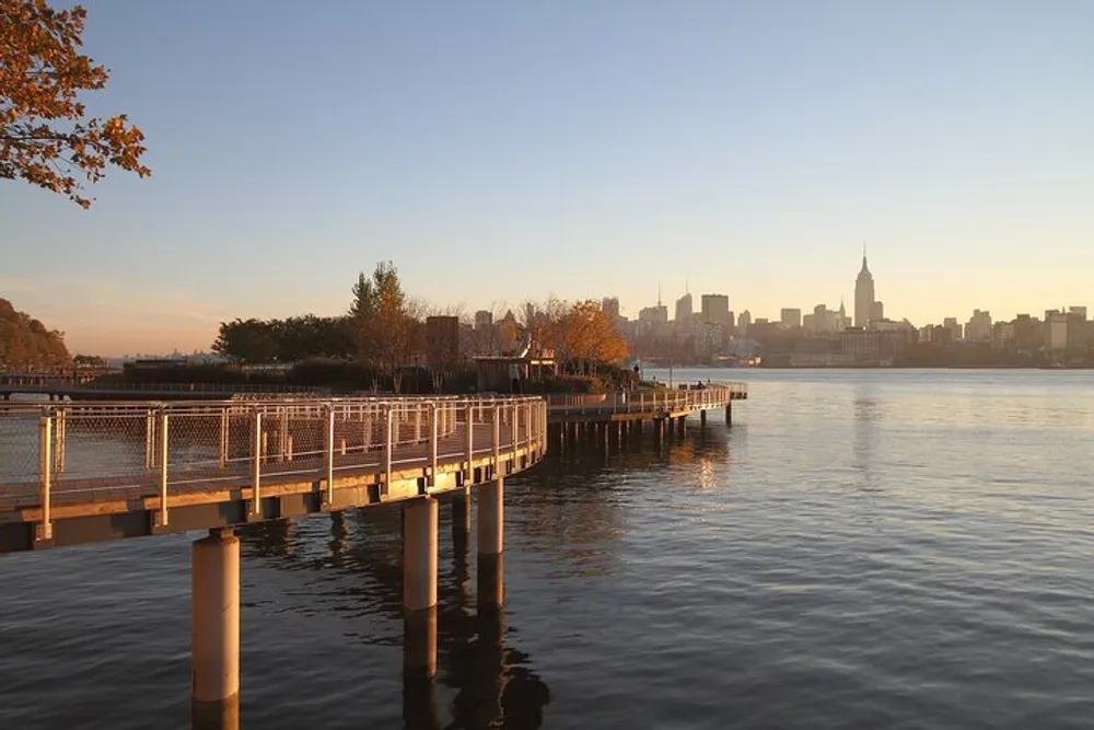 The image shows a serene waterfront pathway at sunset with a view of a city skyline in the background