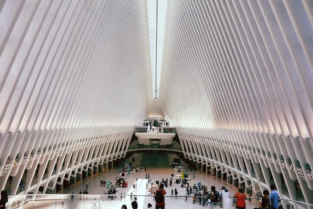 The image shows the interior of the Oculus transportation hub at the World Trade Center with its distinctive white ribbed ceiling and a bustling atrium filled with people