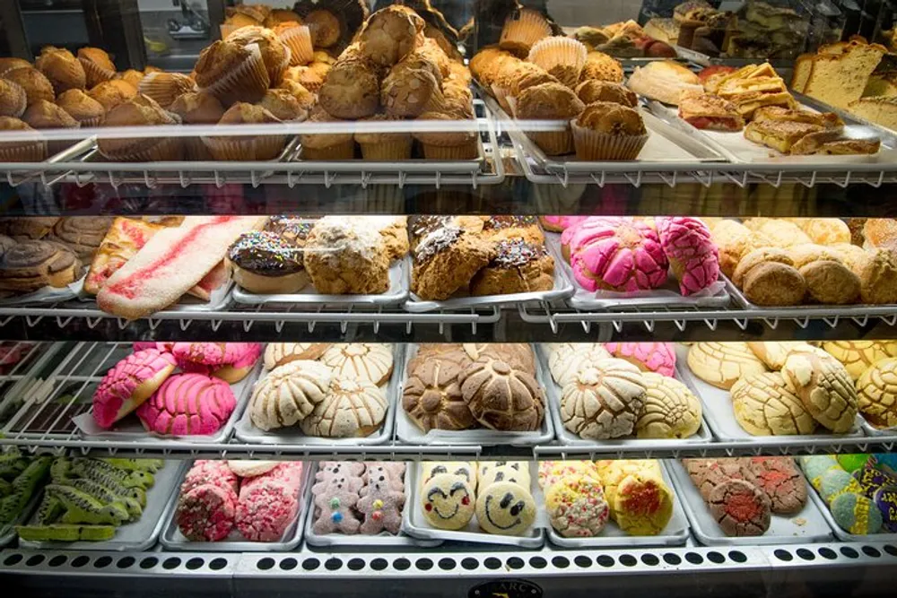 The image shows a variety of colorful and freshly baked pastries displayed in a bakery case tempting customers with their assortment of flavors and shapes