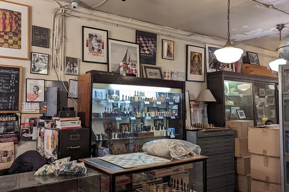 The image shows an eclectic interior possibly of a vintage shop or a collectors space with various items such as framed pictures a chess set and memorabilia displayed on walls and in glass cases
