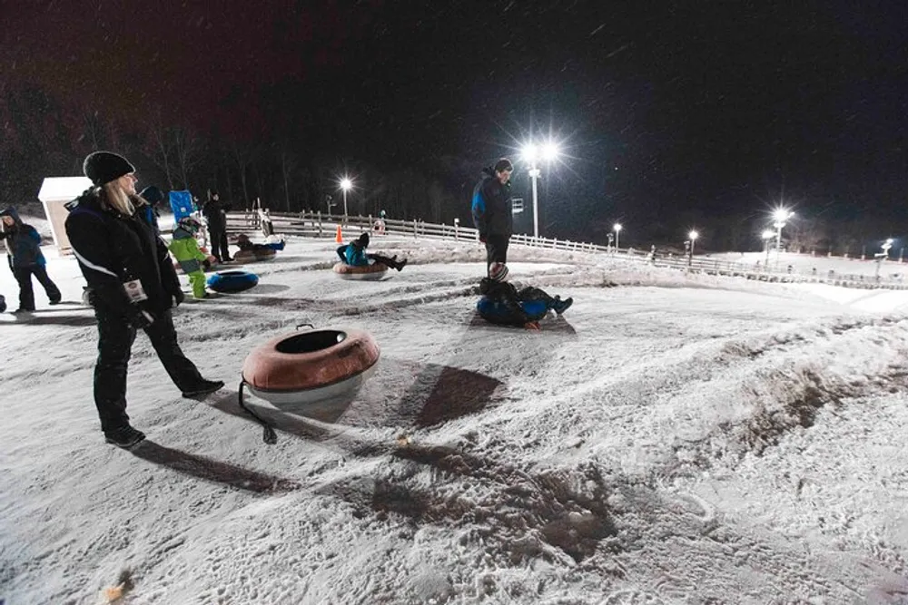 People enjoy a night of snow tubing at a well-lit outdoor winter venue