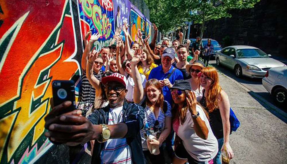 A group of cheerful people are posing for a selfie with a colorful graffiti wall in the background