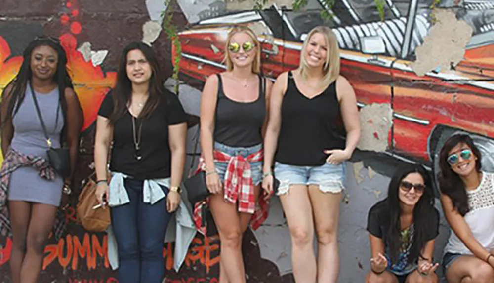 A group of six women is smiling and posing for a photo in front of a colorful graffiti wall