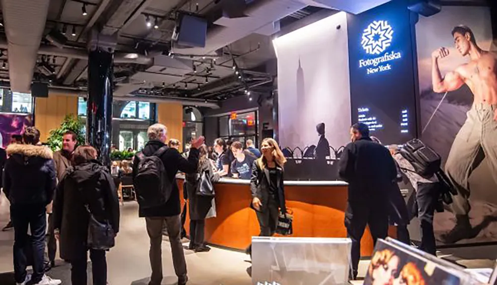 Visitors are gathered inside a modern-looking venue featuring an information desk and large photographic artwork with prominent signage indicating it is at Fotografiska New York