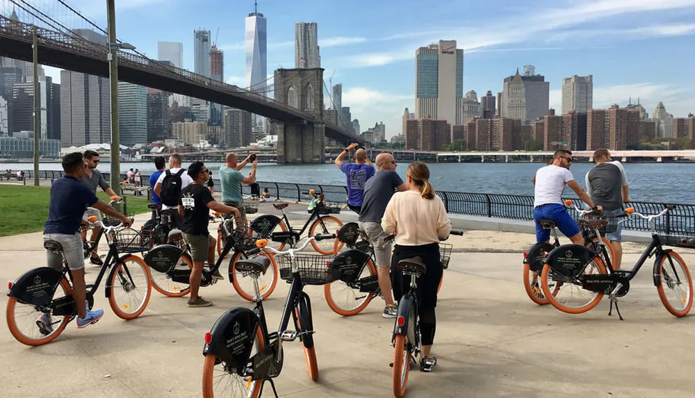 A group of individuals with bikes is enjoying the waterfront view near a bridge in an urban environment
