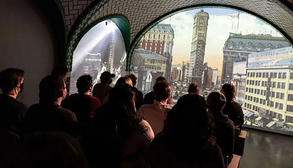A group of people is watching a projection of a historic cityscape inside a room with arched openings