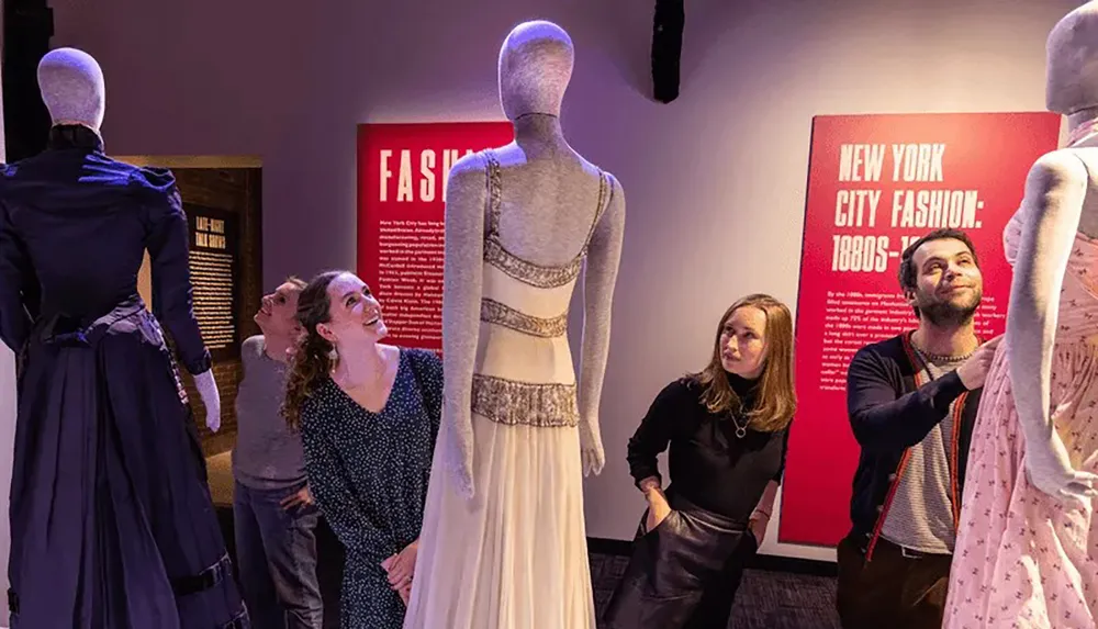 Three people admire historical dresses displayed on mannequins at a fashion exhibition