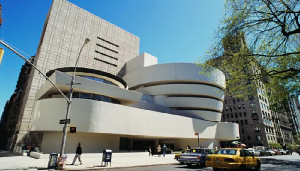 The image shows the Solomon R Guggenheim Museums distinctive architecture with its spiral ramp and white facade with pedestrians and a yellow taxi on the street in front of it