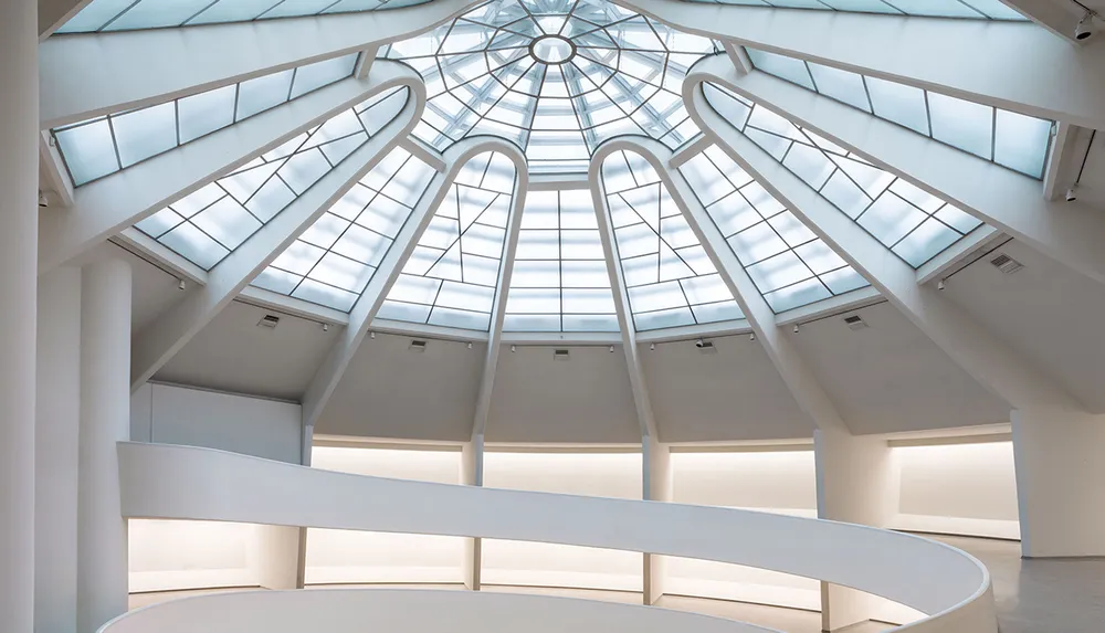 The image shows a modern architectural interior with a white spiral ramp under a striking glass dome and skylights creating a bright and open space