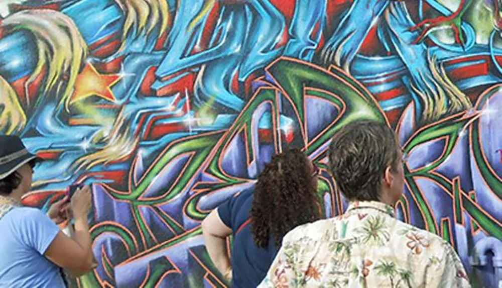 Three people are observing a colorful abstract graffiti wall mural