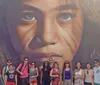 A group of people are standing in front of a colorful mural featuring stylized animal faces
